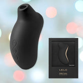 A black LELO SONA Cruise Sonic Wave Clitoral Massager is displayed against a soft, bokeh background. The image includes the massager itself and its packaging, showcasing the device nestled in a sleek black box with gold accents and the product name. This elegant massager features Sonic Pulse technology for enhanced pleasure settings.